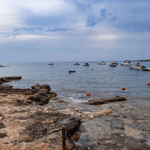 Armier Bay 1 A rugged and rocky coastline with boats dotting the horizon with an overcast sky.