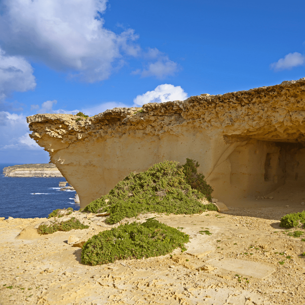 A limestone outcrop with carved chambers overlooking the sea and cliffs in Gozo.